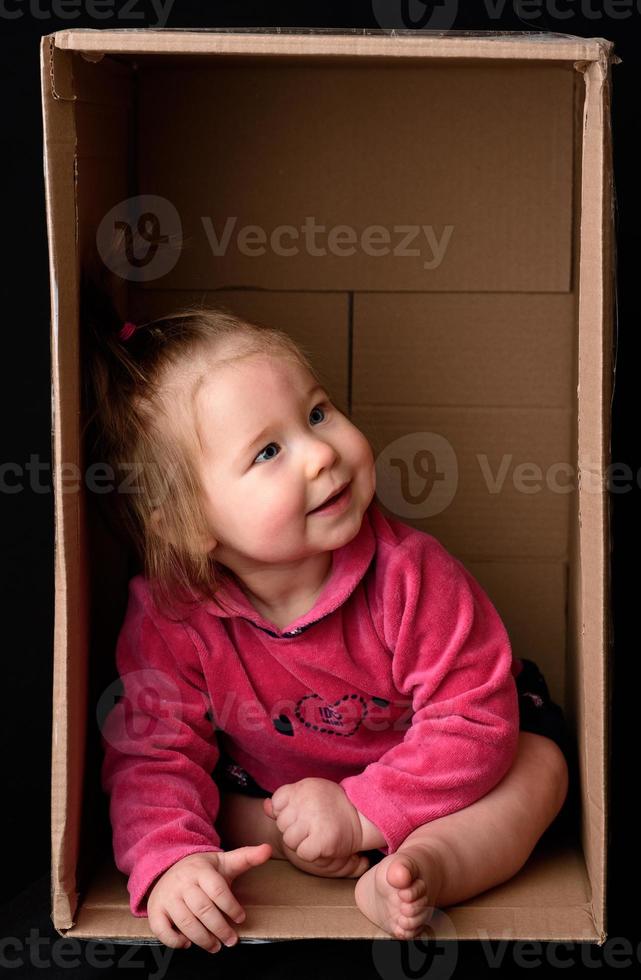 Little cute, beautiful girl sits in a box. photo