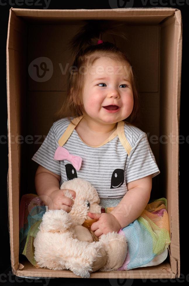 una niña linda y hermosa se sienta en una caja. foto