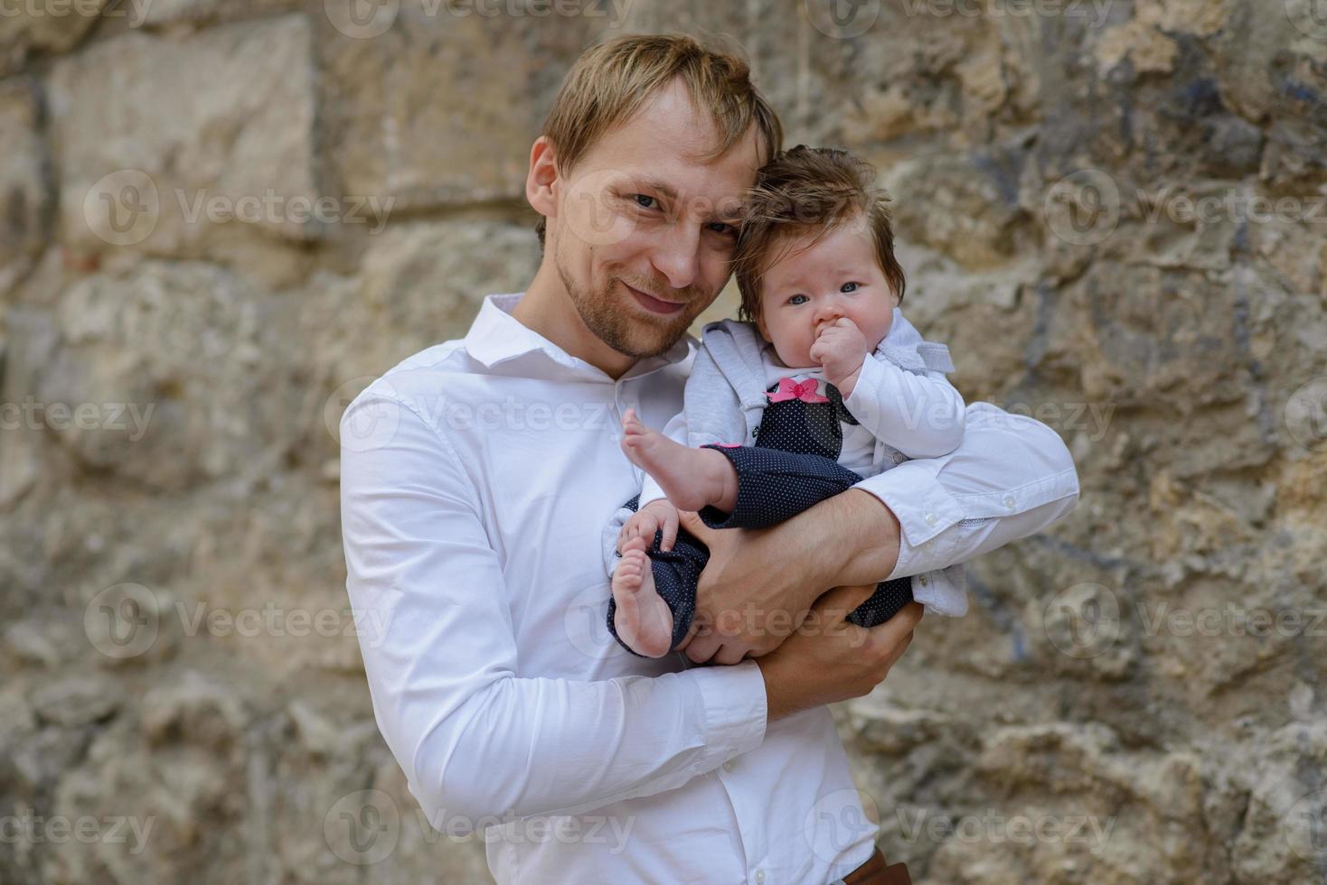 portrait of young father holding crying baby girl over white brick wall photo