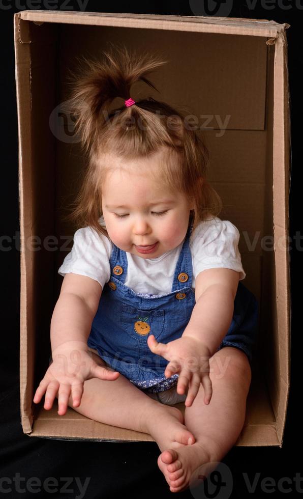 una niña linda y hermosa se sienta en una caja. foto