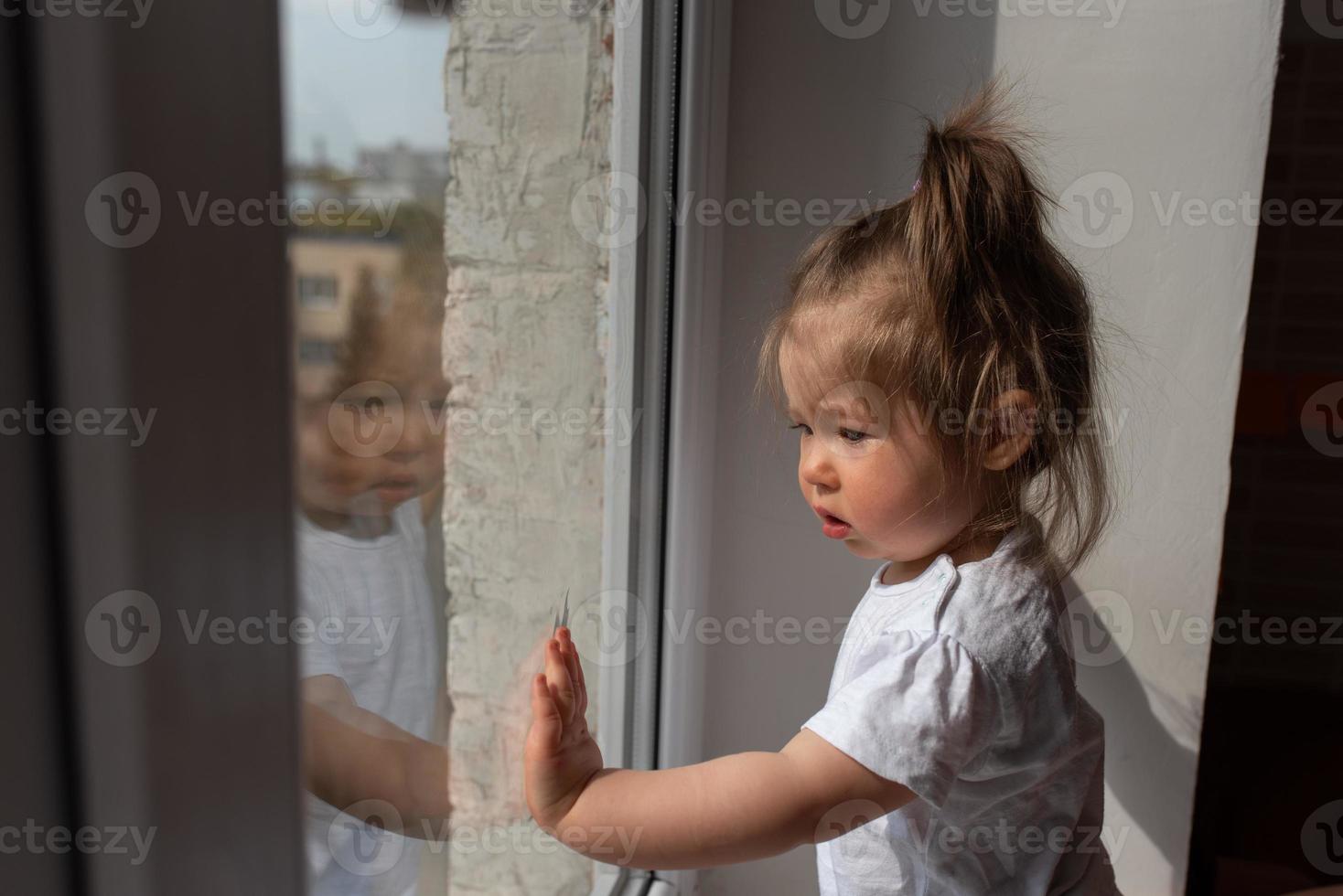 la niña mira por la ventana y pregunta afuera durante la cuarentena causada por el coronavirus. foto