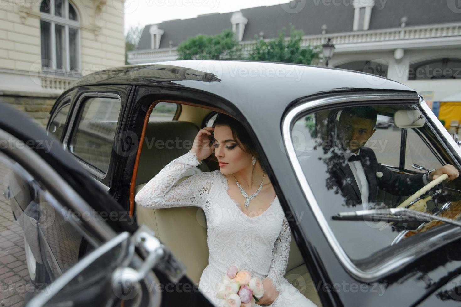 Beautiful happy young bride and groom looking from retro auto photo