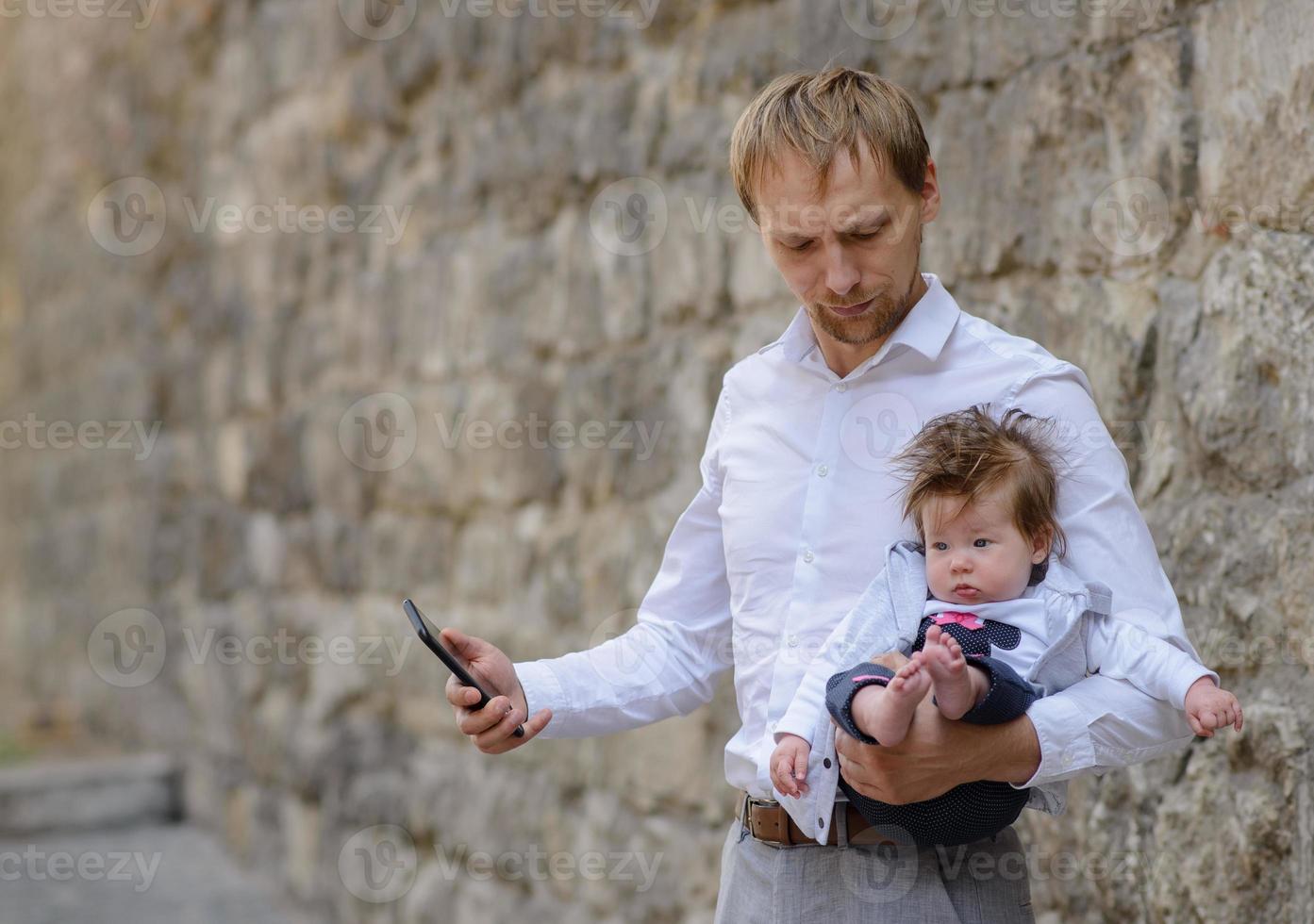 A young father is talking on a cell phone and holds his little daughter in his arms. copy space photo