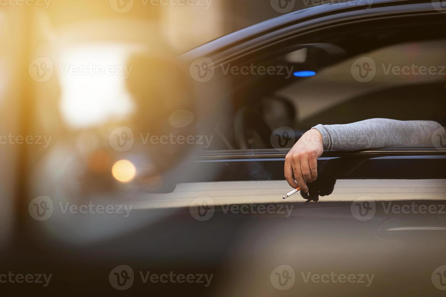 Hand hold cigarratte by fingers outside car on traffic jouney photo