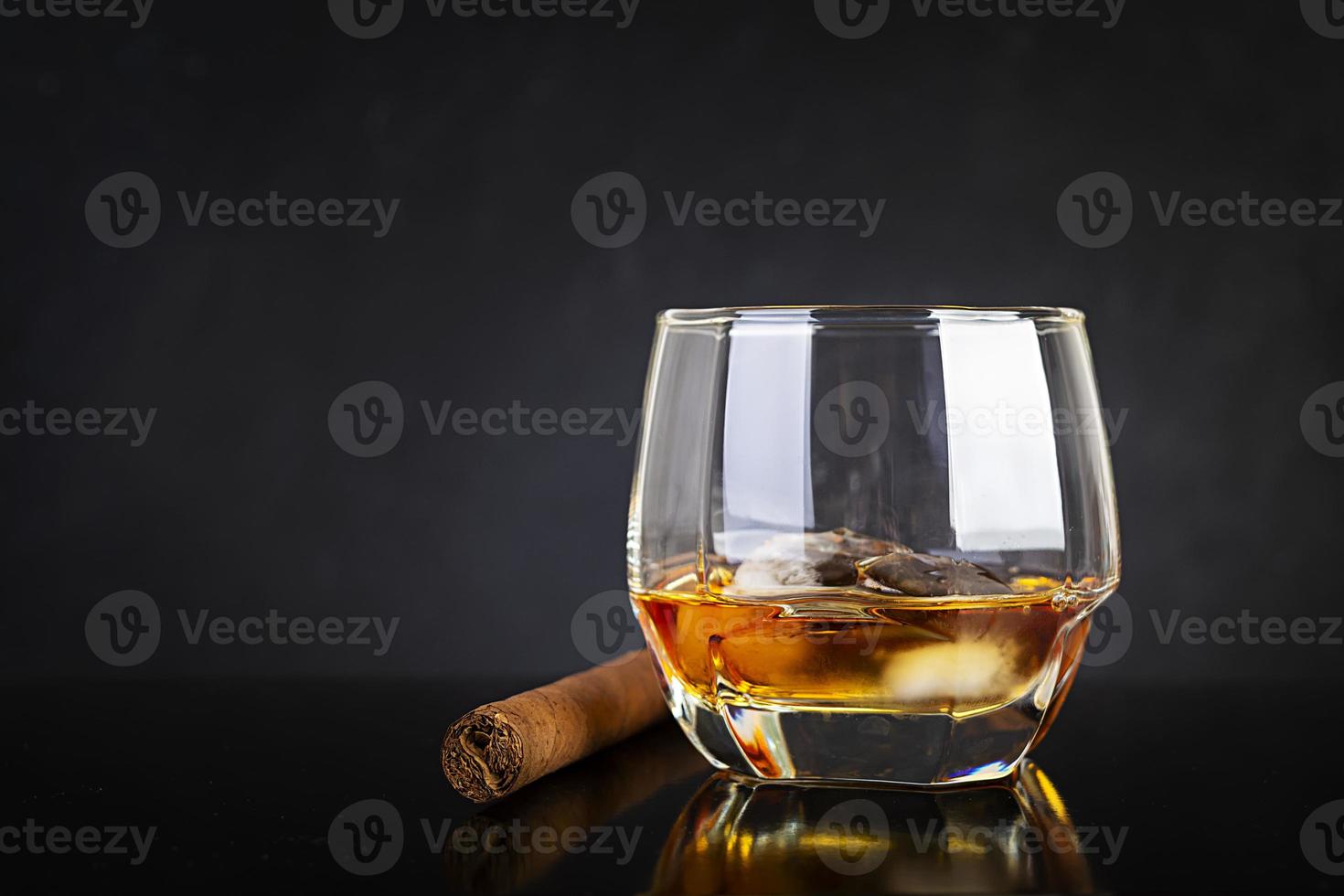 Glass of whiskey and cigar on dark background. photo