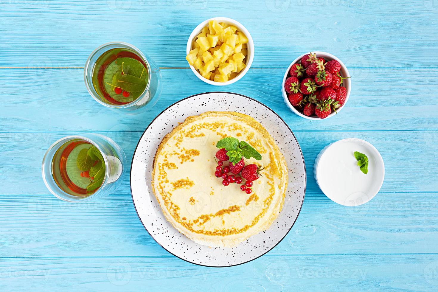 Pancakes with caramelized apples, raspberries, strawberries and red currants. Brunch with green tea and crepes. photo