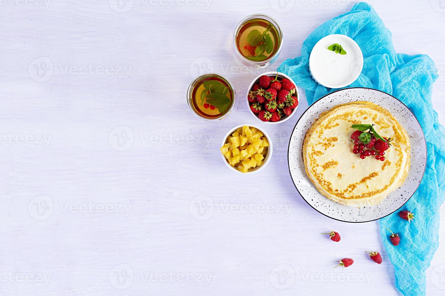 Pancakes with caramelized apples, raspberries, strawberries and red currants. Brunch with green tea and crepes. photo