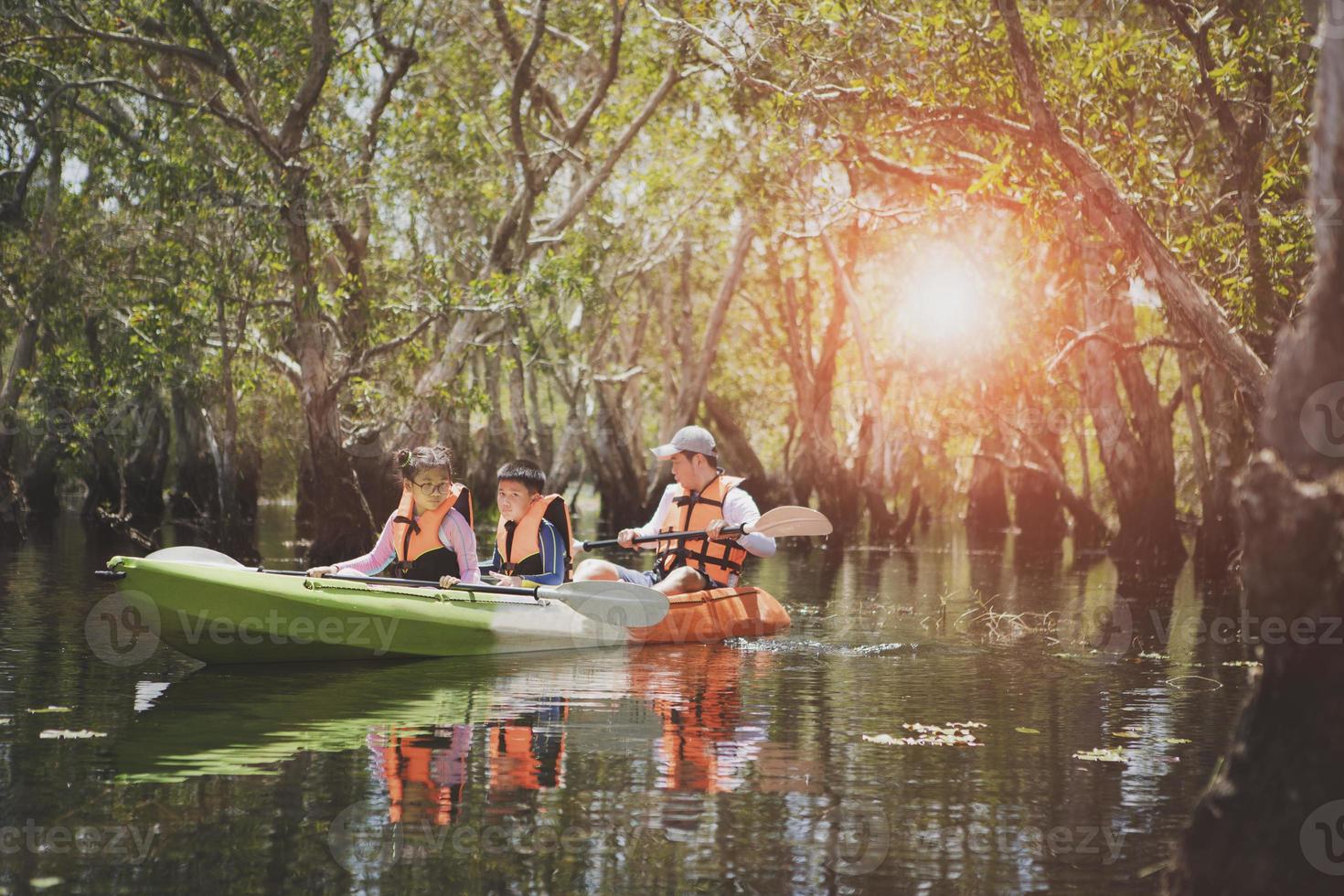 familia asiática navegando en kayak de mar en un bosque de manglares foto