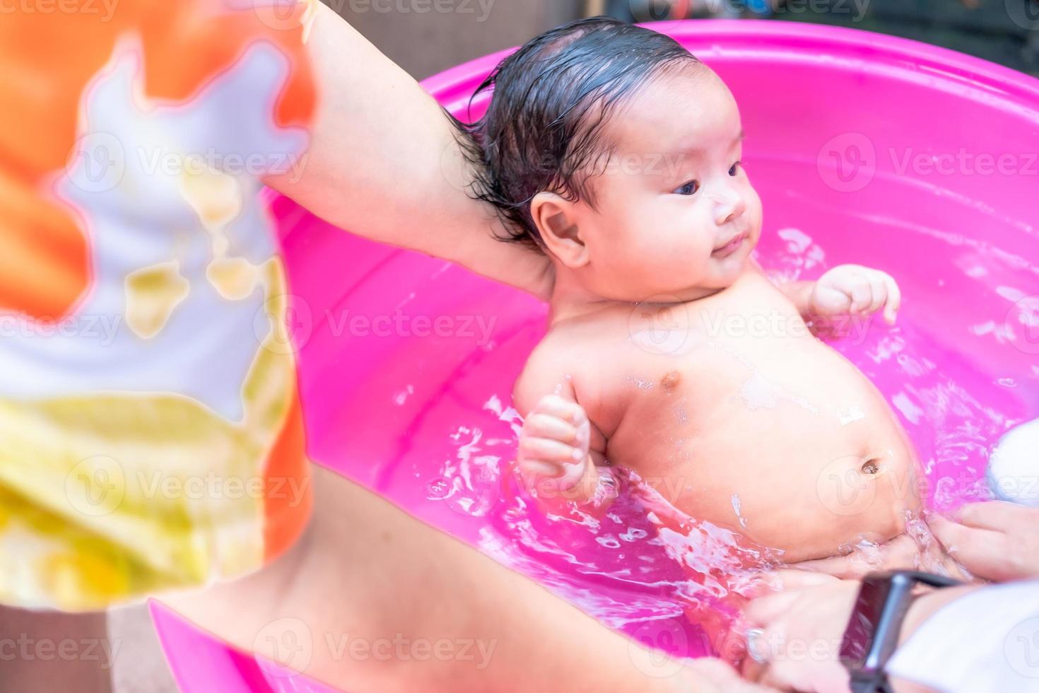 mamá asiática ducha al bebé para limpiar la suciedad dar al niño en un  recipiente de