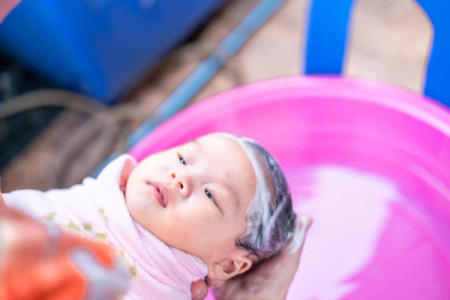 mamá asiática ducha al bebé para limpiar la suciedad dar al niño en un  recipiente de