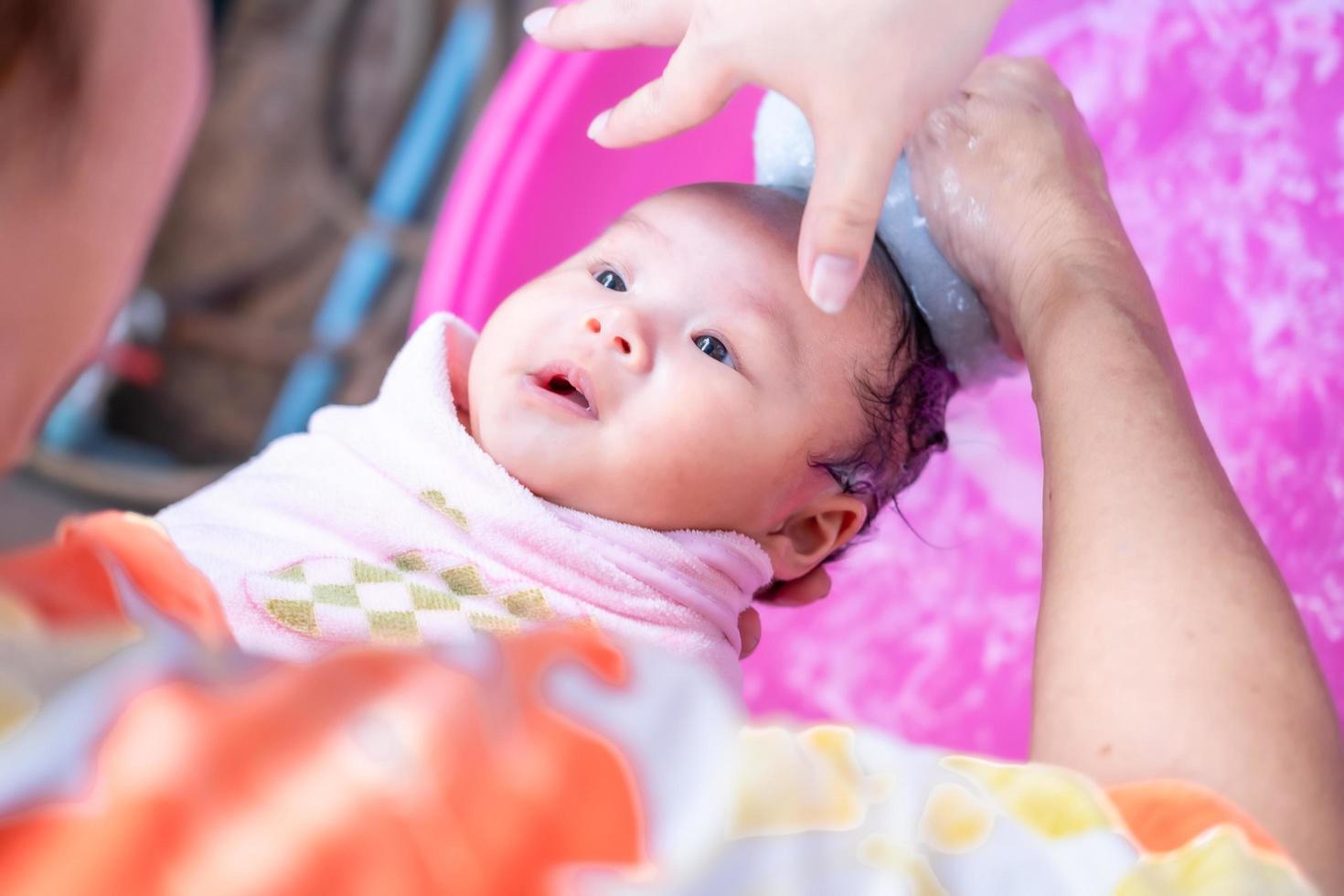 mamá asiática ducha al bebé para limpiar la suciedad dar al niño en un recipiente de baño para la limpieza estilo de vida familiar entre la madre y el niño utilizado para la ducha del bebé productos de crema champús lociones y productos para el cuidado del bebé foto