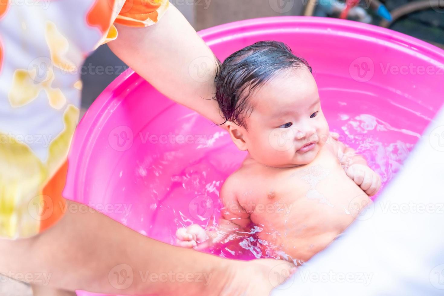 mamá asiática ducha al bebé para limpiar la suciedad dar al niño en un  recipiente de