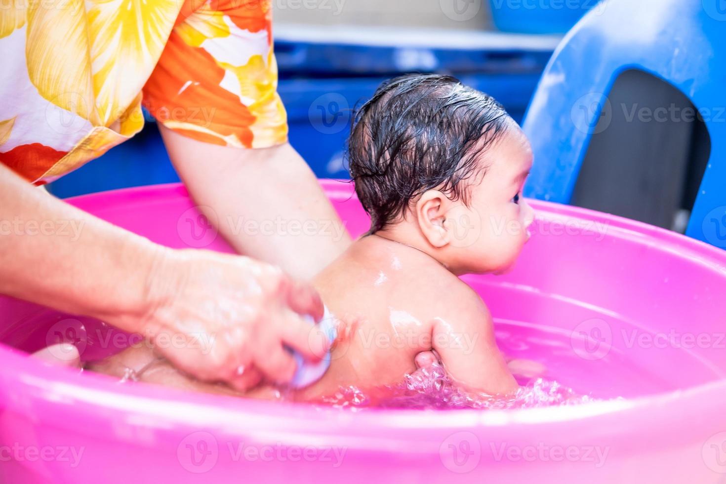 mamá asiática ducha al bebé para limpiar la suciedad dar al niño en un  recipiente de