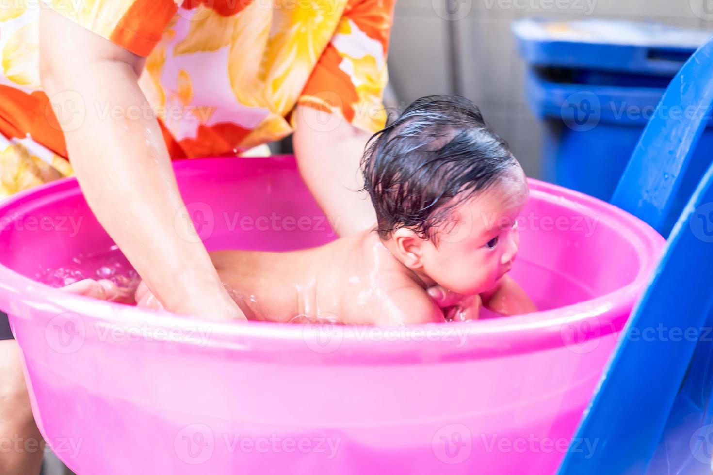 mamá asiática ducha al bebé para limpiar la suciedad dar al niño en un  recipiente de