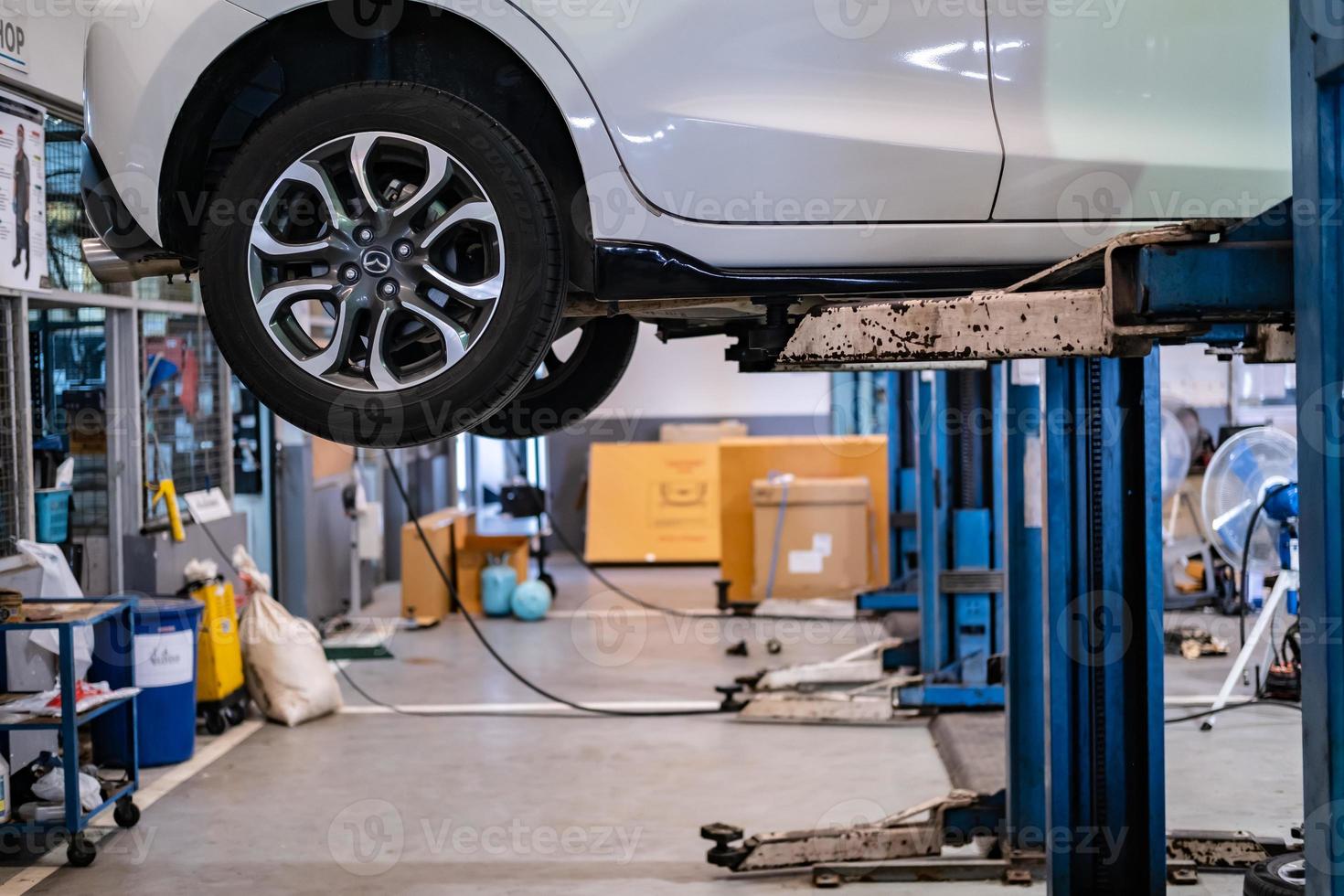 BANGSAEN THAILAND MAR 2022 This car mazda 2 brand japan waiting for repair on car Lift in garage dealership on room customer parked in showroom of thailand for Illustrative editorial image. photo