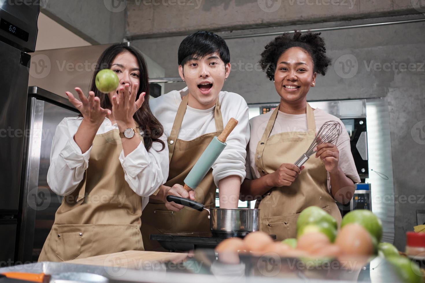 tres jóvenes estudiantes en clase de cocina usan delantales disfrutan y son alegres y divertidos con ingredientes y herramientas en la cocina, sonríen felices, preparan frutas para aprender juntos un curso culinario divertido. foto