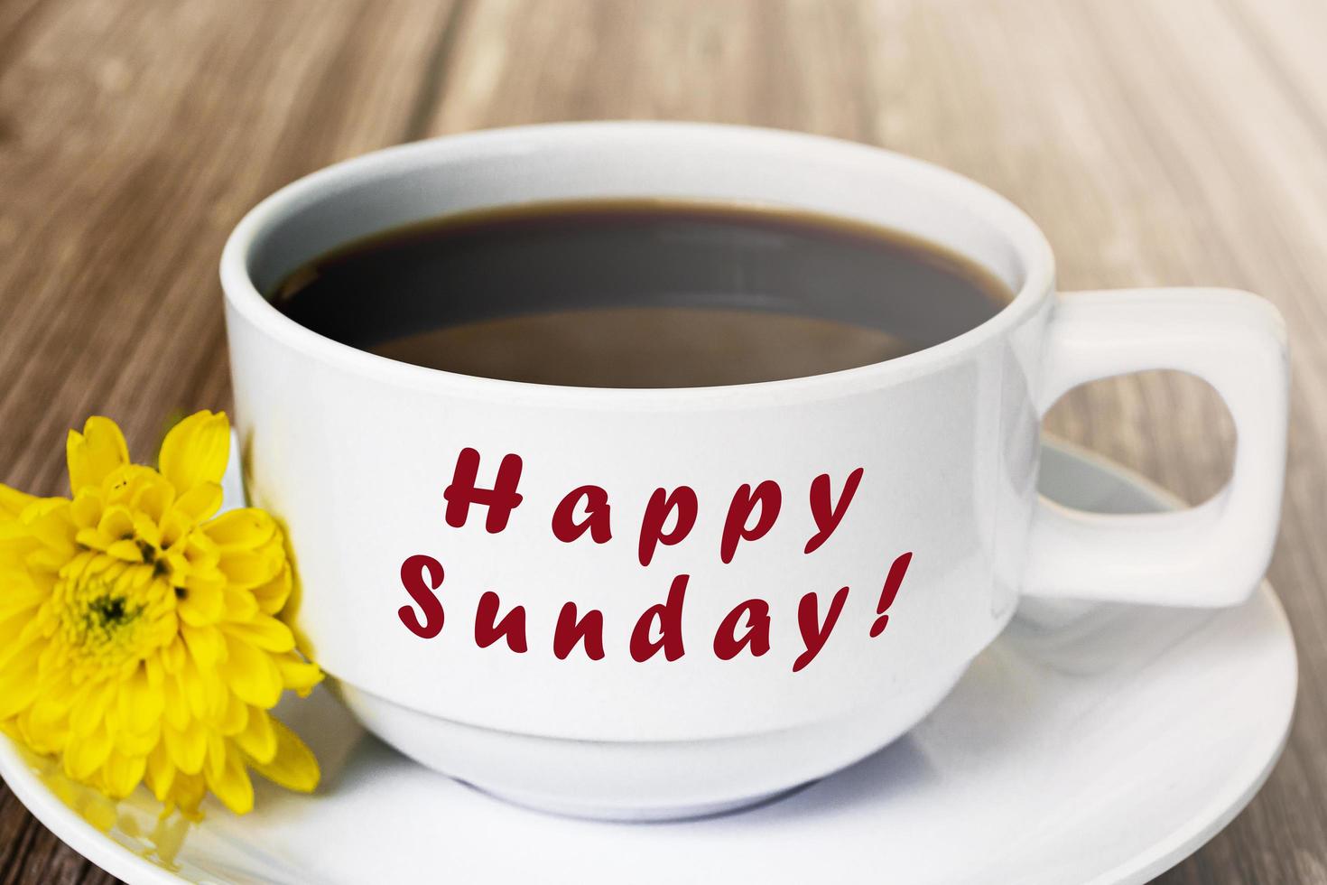 Happy sunday text on white coffee cup with yellow flower on wooden desk. photo