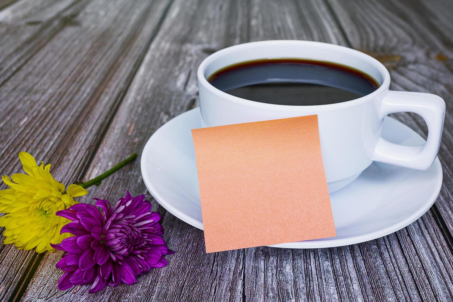 Sticky note with white coffee cup and flowers on wooden desk. For copy space. photo