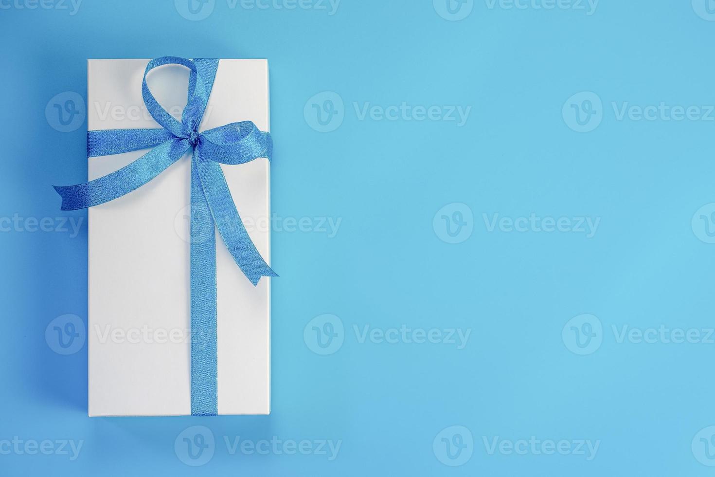 White gift box with blue ribbon on blue background photo