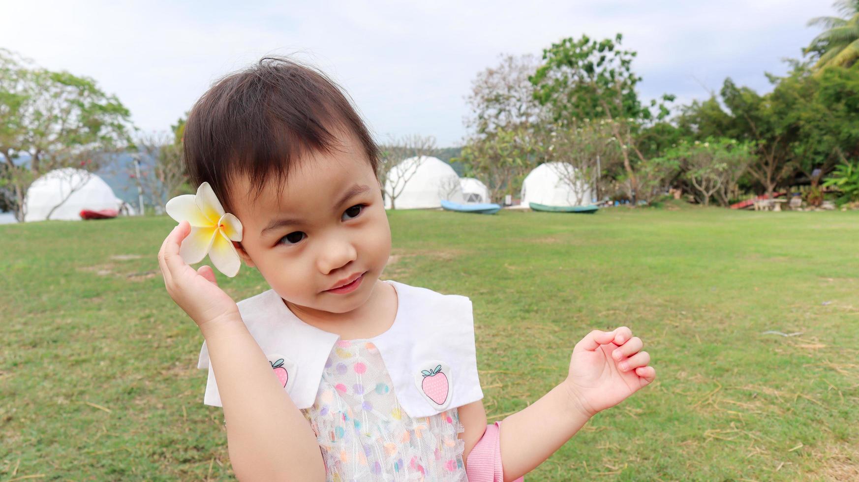 Niña caucásica asiática de 3 años con flor amarilla blanca en la oreja. foto