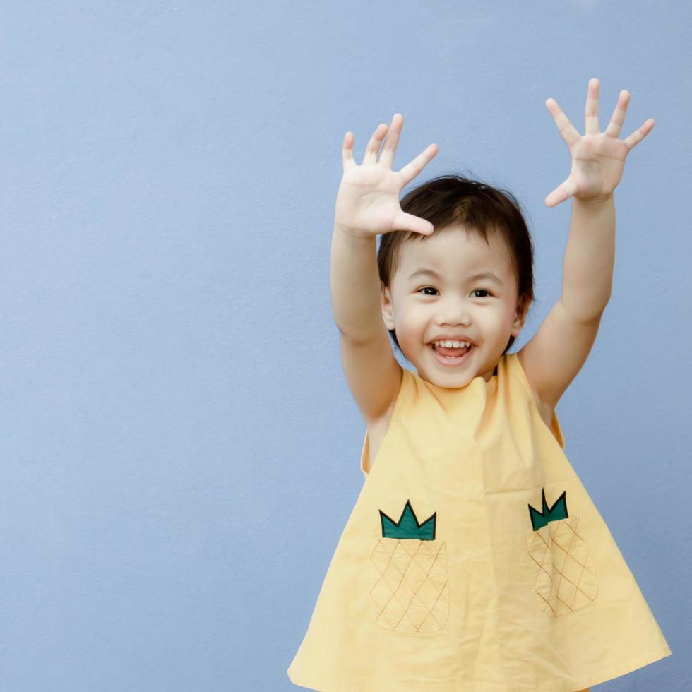 retrato de feliz y encantadora niña asiática de 3 años, pequeña niña pequeña levantando la mano foto