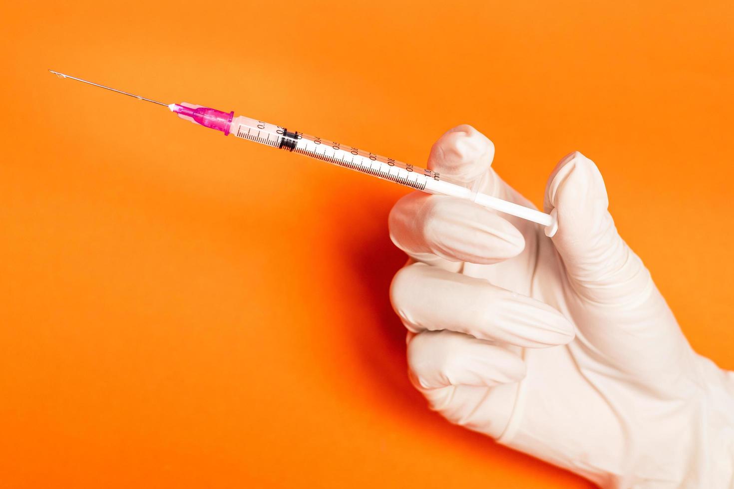 Hand in white gloves holding syringe on oragne background with copy space photo