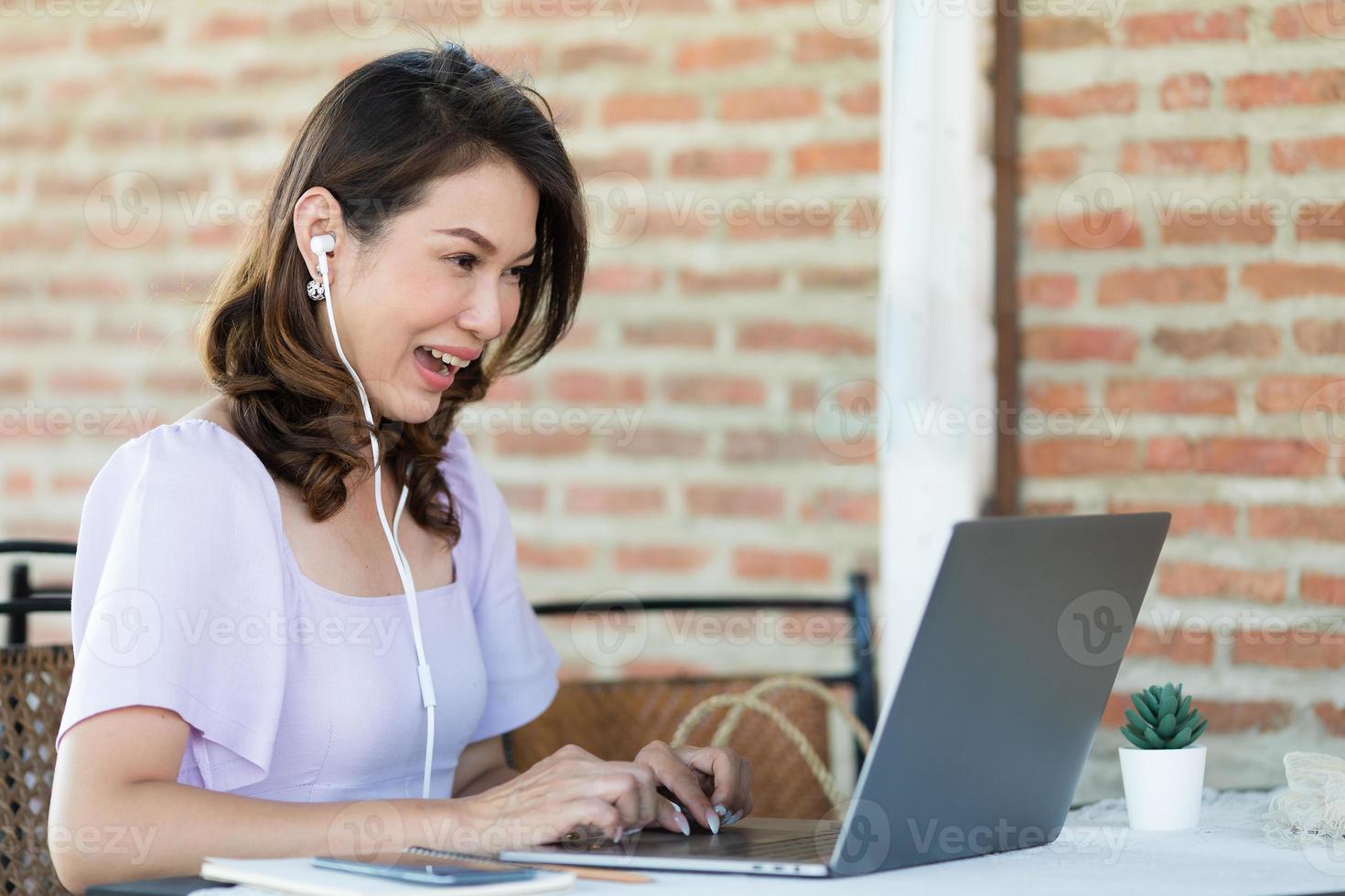 The beautiful middle-aged woman sitting in food shop and working with laptop notebook computer and feel excited with good news on screen. Freelancer job and work from anywhere concept photo
