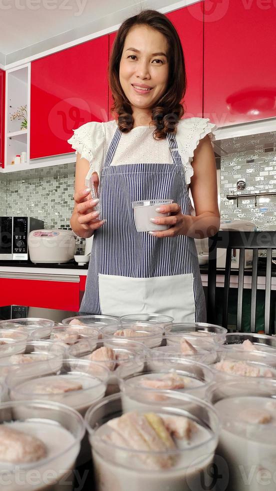 Beautiful Asian housewife prepares set of banana in coconut milk, famous native Thai style dessert, for sale and delivery to customers. The concept for small and medium entrepreneur working at home photo