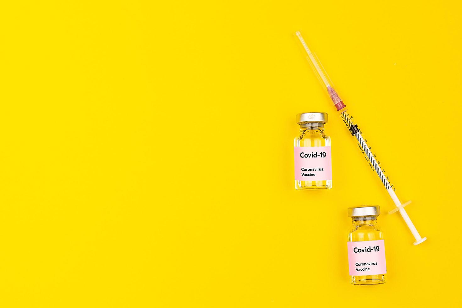 Covid-19 coronavirus vaccine bottles and syringes put together on yellow background with copy space. Top view and flat lay shot photo