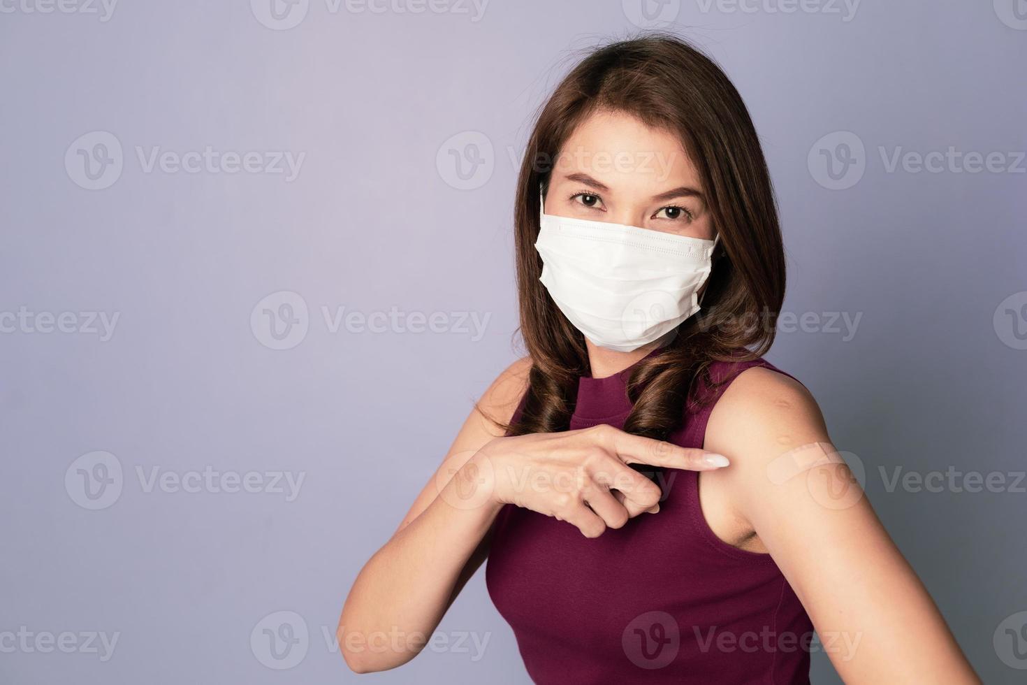 Vaccinated Asian woman wearing protective face mask point finger showing plaster bandage on arm after a coronavirus vaccine injection, Covid-19 vaccination, and antiviral Immunization concept photo