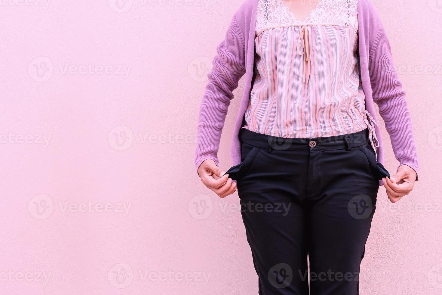 Woman showing her empty pockets on concrete wall background. photo