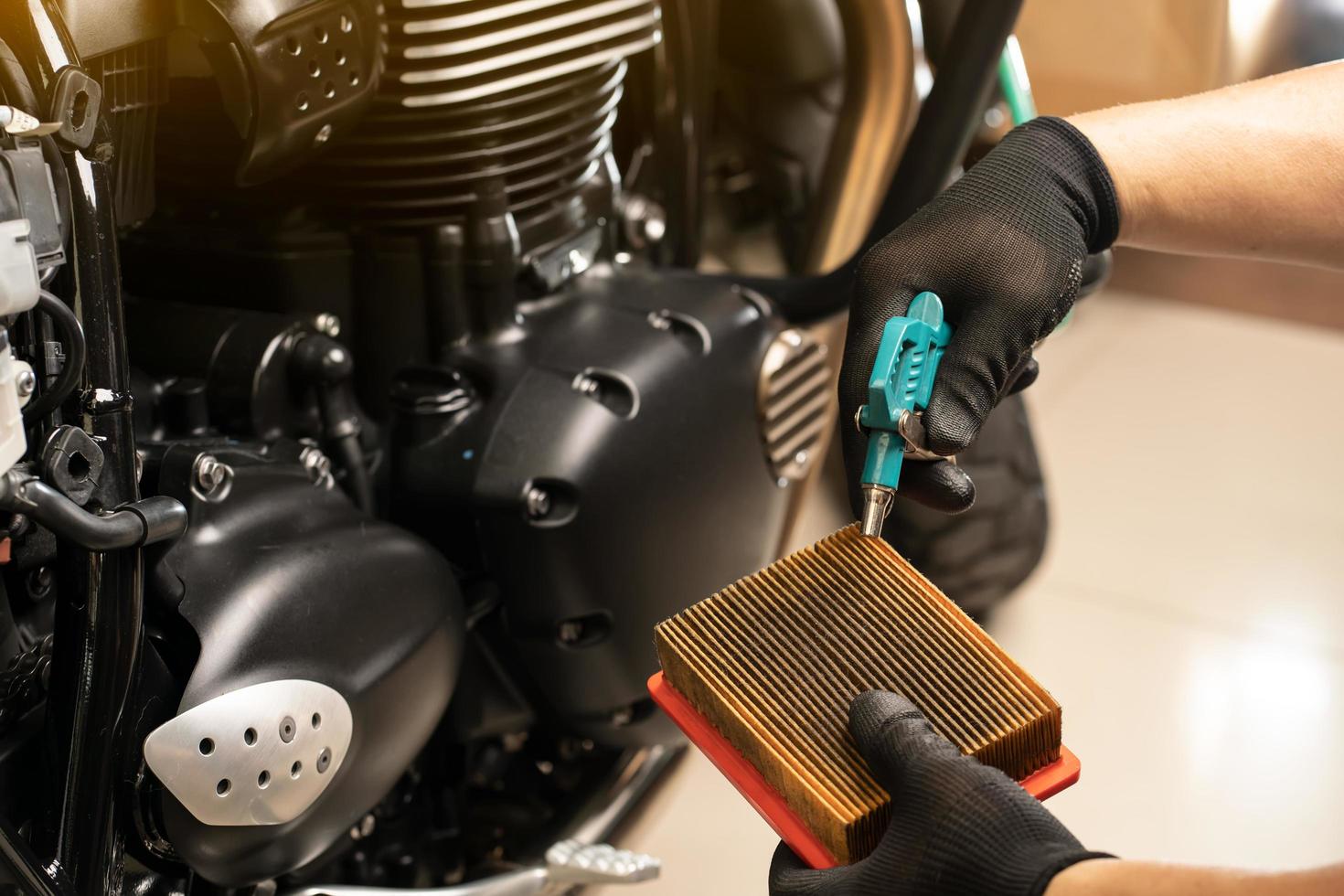 mechanic holding dirty Engine Air Filter over motorcycle and cleaning Filter with air blow gun .mechanic working in motorcycle garage. Repair service and maintenance concept photo