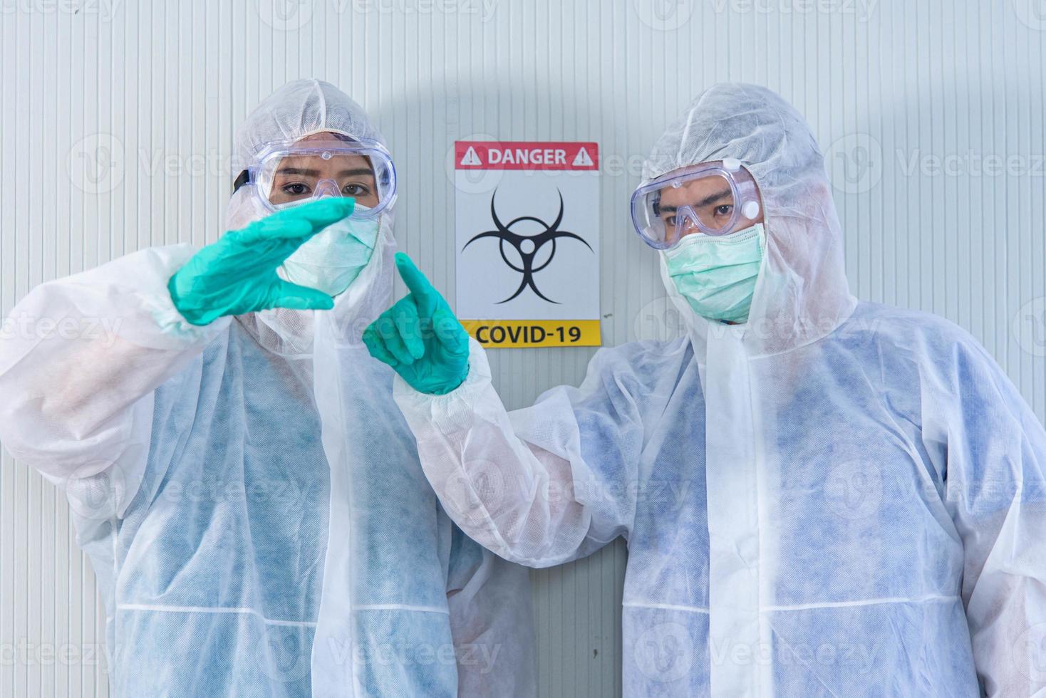 Two ASIAN medical staffs wear PPE suit and medical gloves showing  something in the air  in quarantine room photo
