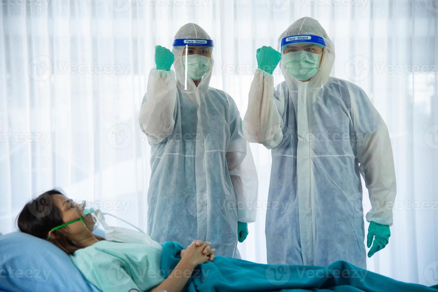 Two medical staffs with PPE suit and facial mask standing and hand up for fighting beside aging woman patient infected with CORONA VISRUS or COVID-19 bedroom in quarantine room at the hospital. photo