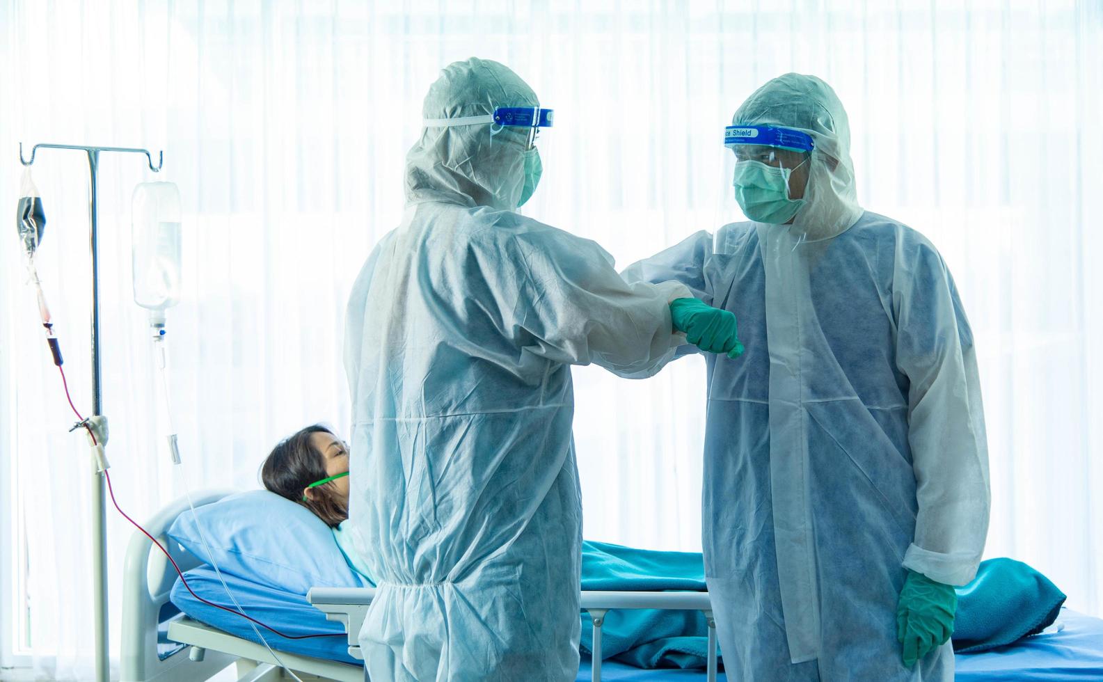 dos miembros del personal médico con traje de ppe y máscara facial parados en un brazo plegable junto a una paciente anciana infectada con corona visrus o dormitorio covid-19 en la sala de cuarentena del hospital. foto