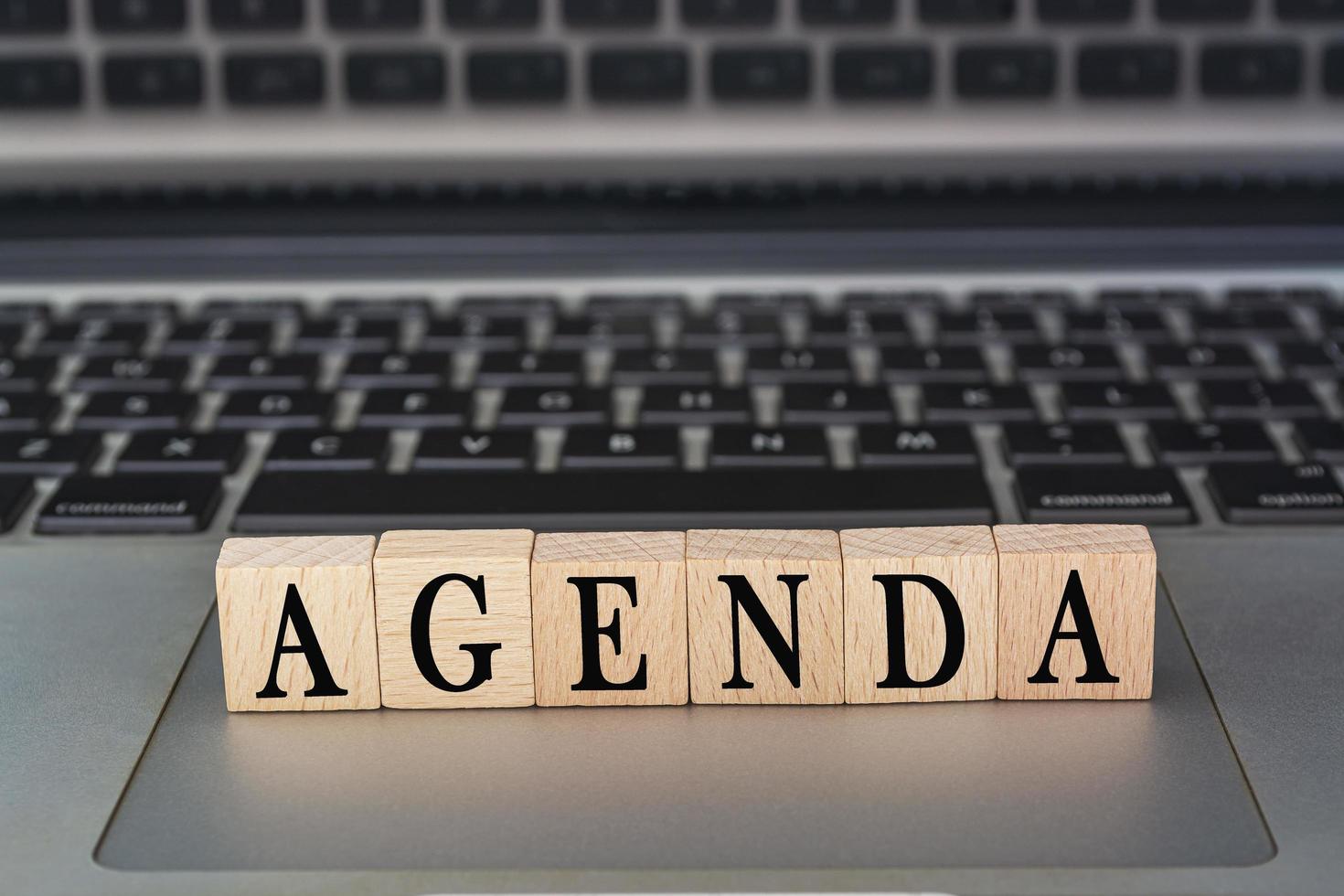 Agenda text on wooden block placed on laptop or notebook. Meeting concept. photo