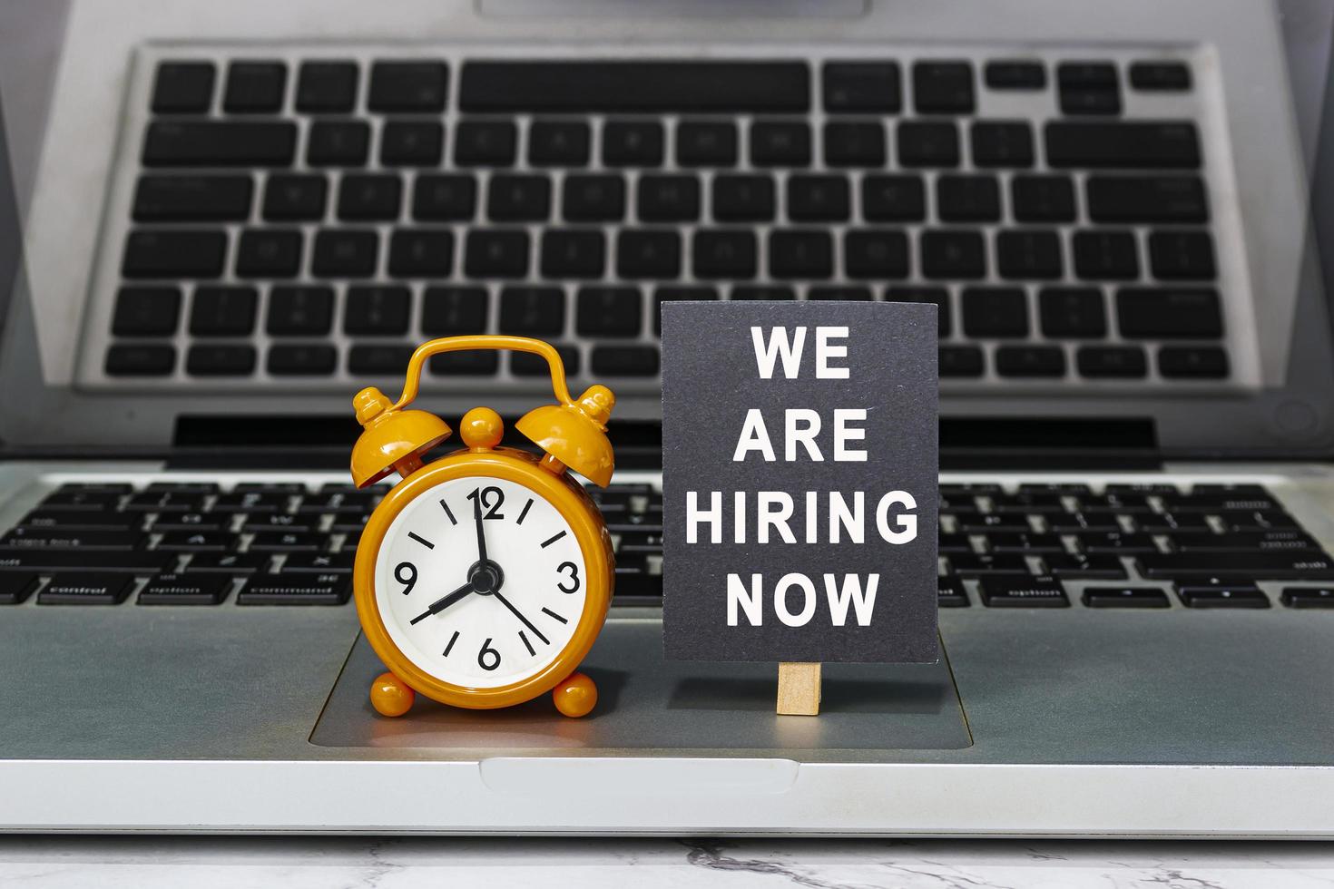 We are hiring now text on chalkboard with clock set at 8 o'clock on a laptop. photo