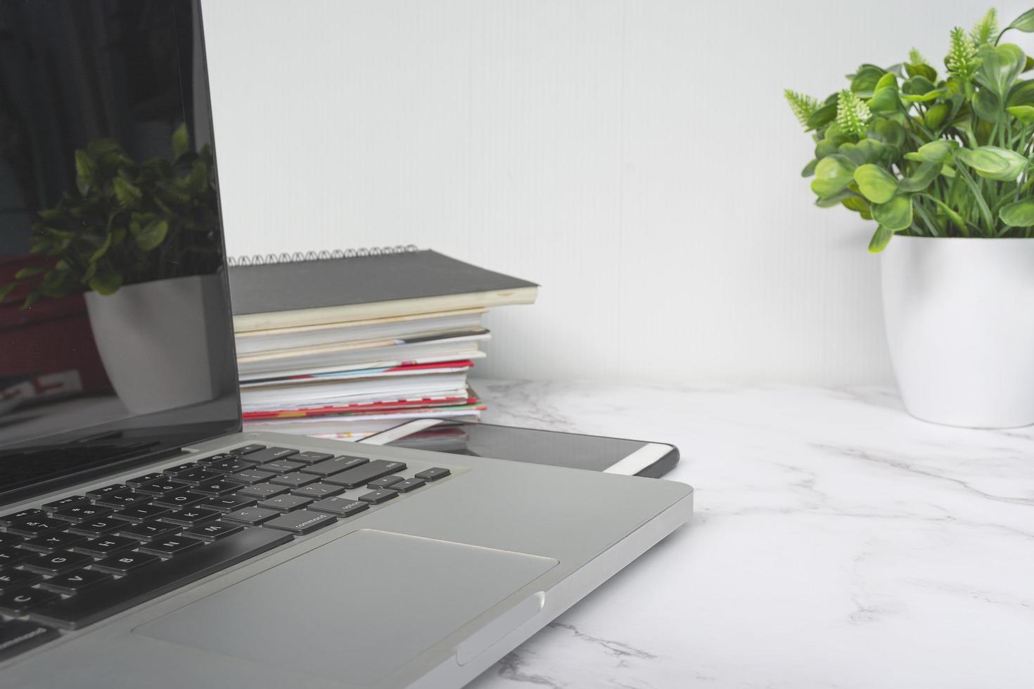 Laptop on white table with potted plant, notebooks and smartphone. photo