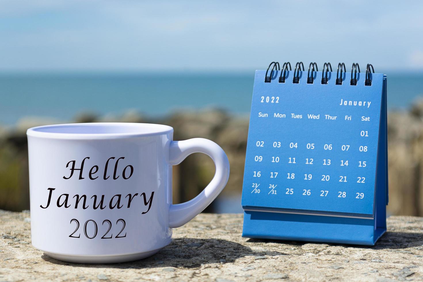 hola hola enero de 2022 escrito en una taza de café blanca con calendario azul foto