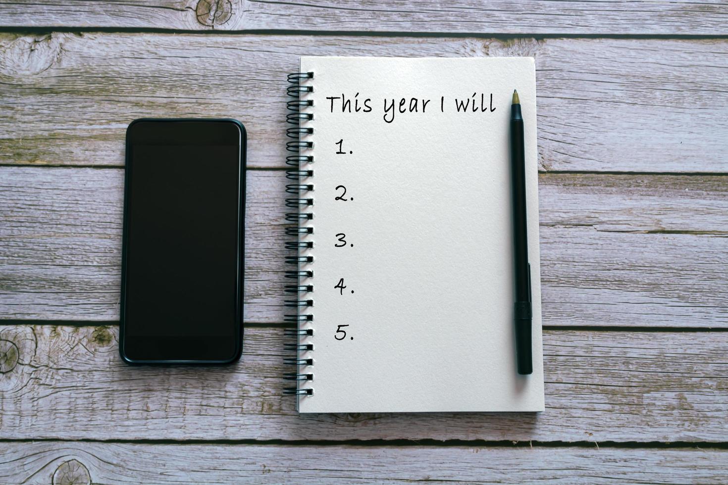 This year I will text on notepad on wooden background with smartphone and pen. photo