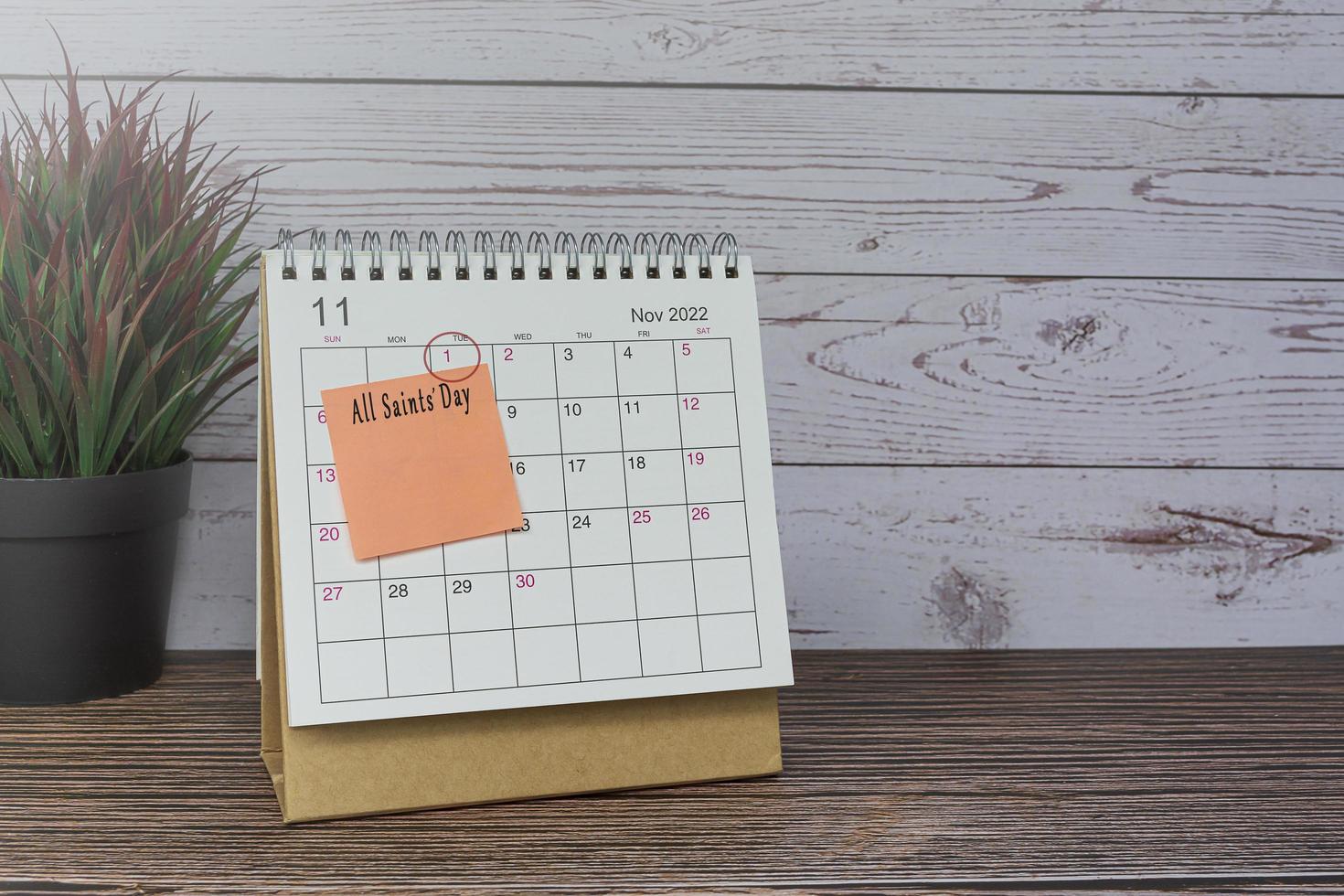 November 2022 calendar on wooden desk with date circle and text on sticky note. photo
