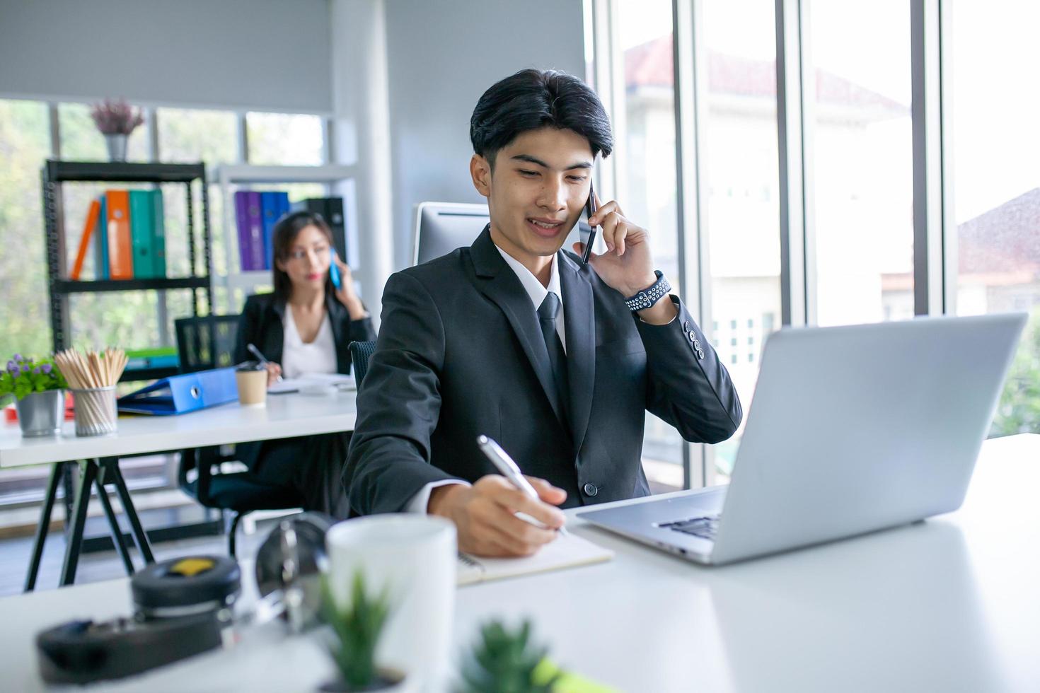 Portrait of Asian handsome man working at the office, using smartphone and computer on table. photo