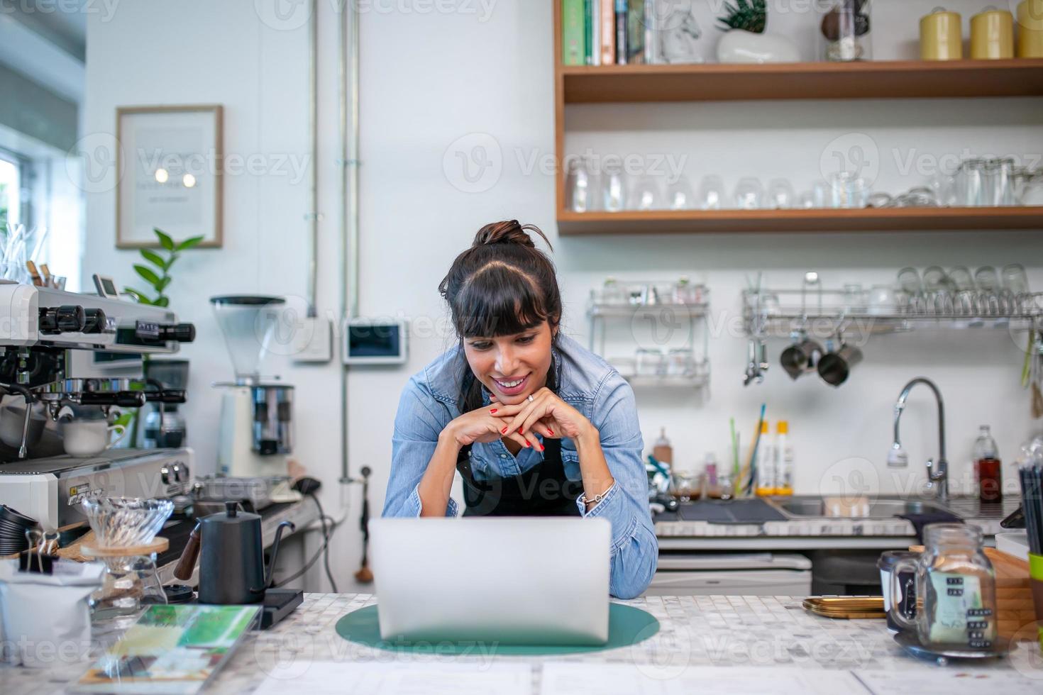 mujer feliz barista usando una computadora portátil para tomar el pedido del cliente en la cafetería. foto