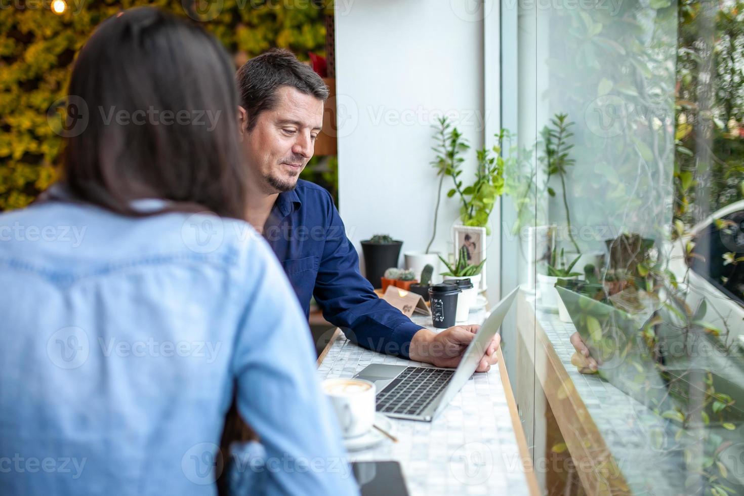 colegas hablando y usando portátiles trabajan juntos en la cafetería. foto