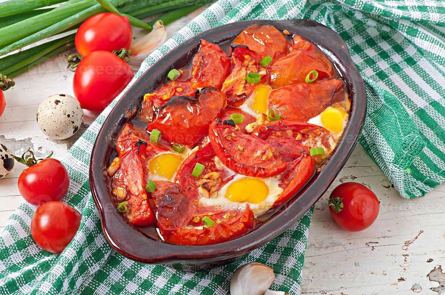 Baked tomatoes with garlic and eggs decorated with green onions photo