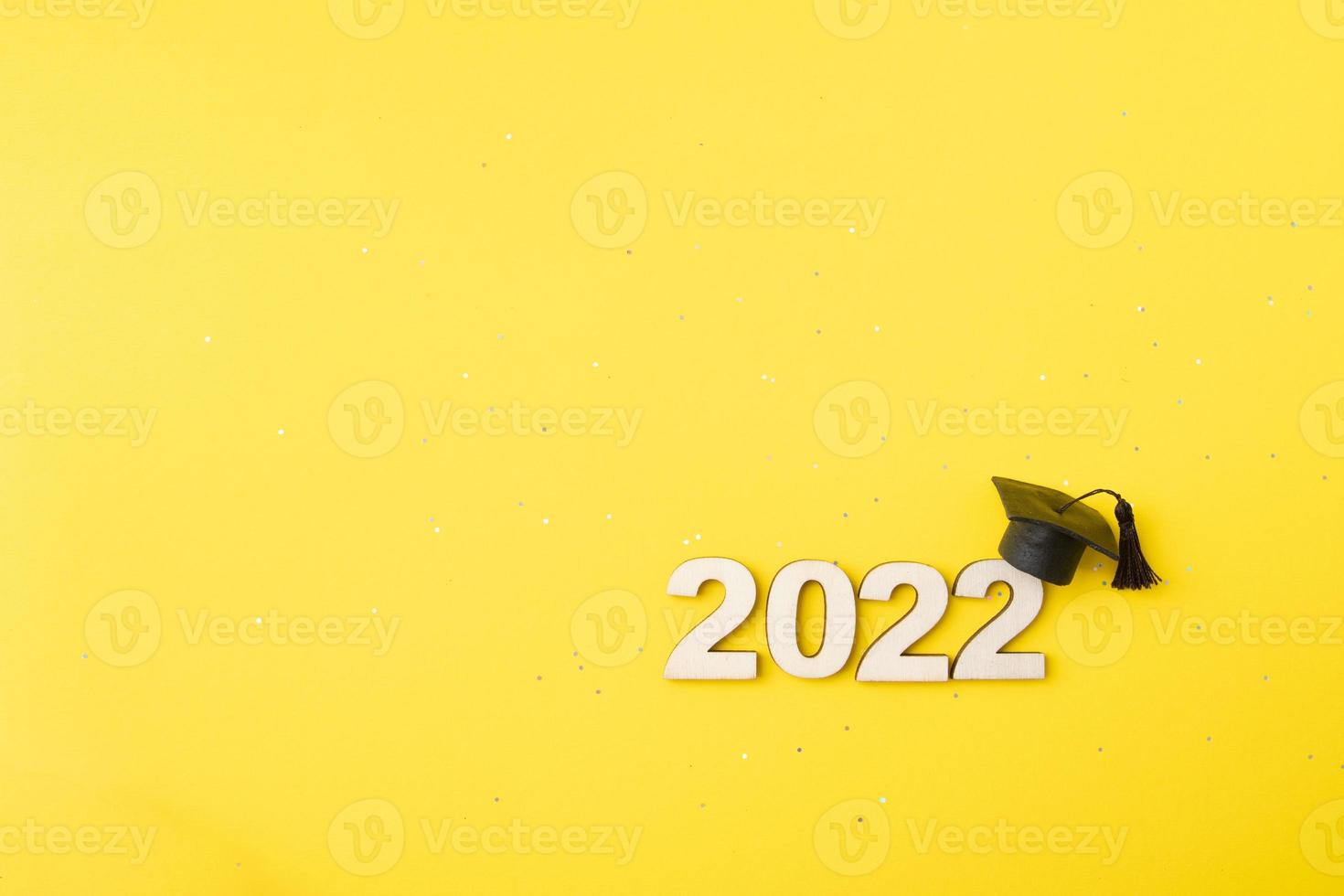 Graduated hat or cap with wooden number 2022 on a yellow glitter background. Class 2022 concept photo