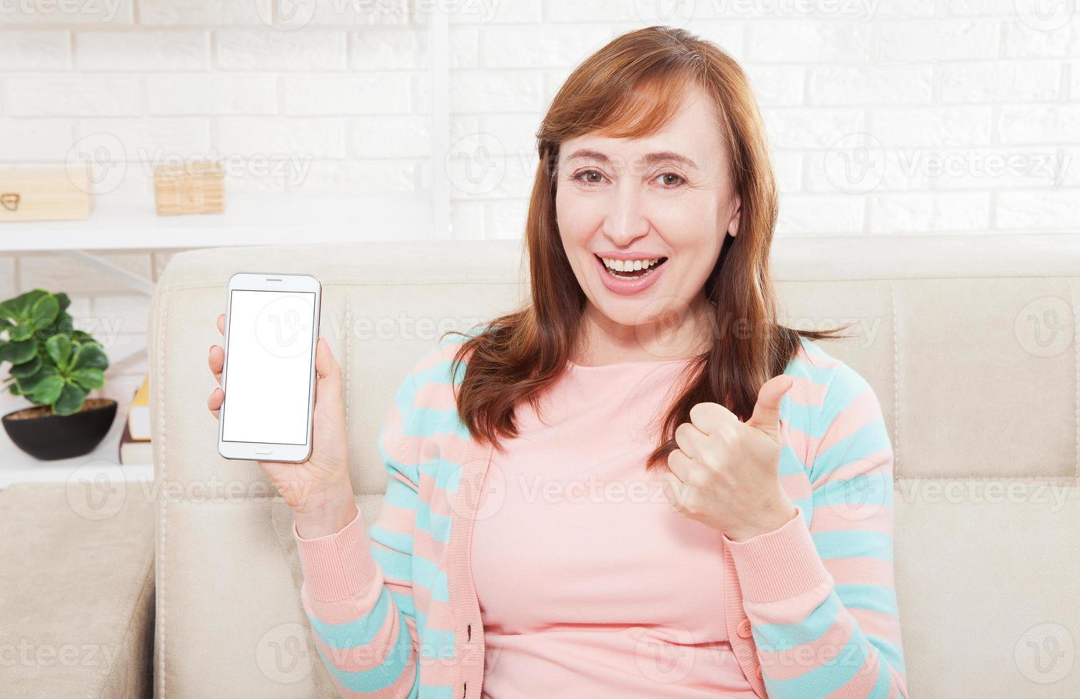 Female hand holding white phone on white clipping path inside at home background. Middle age woman. Copy space and mock up. Happy person, thumb up photo