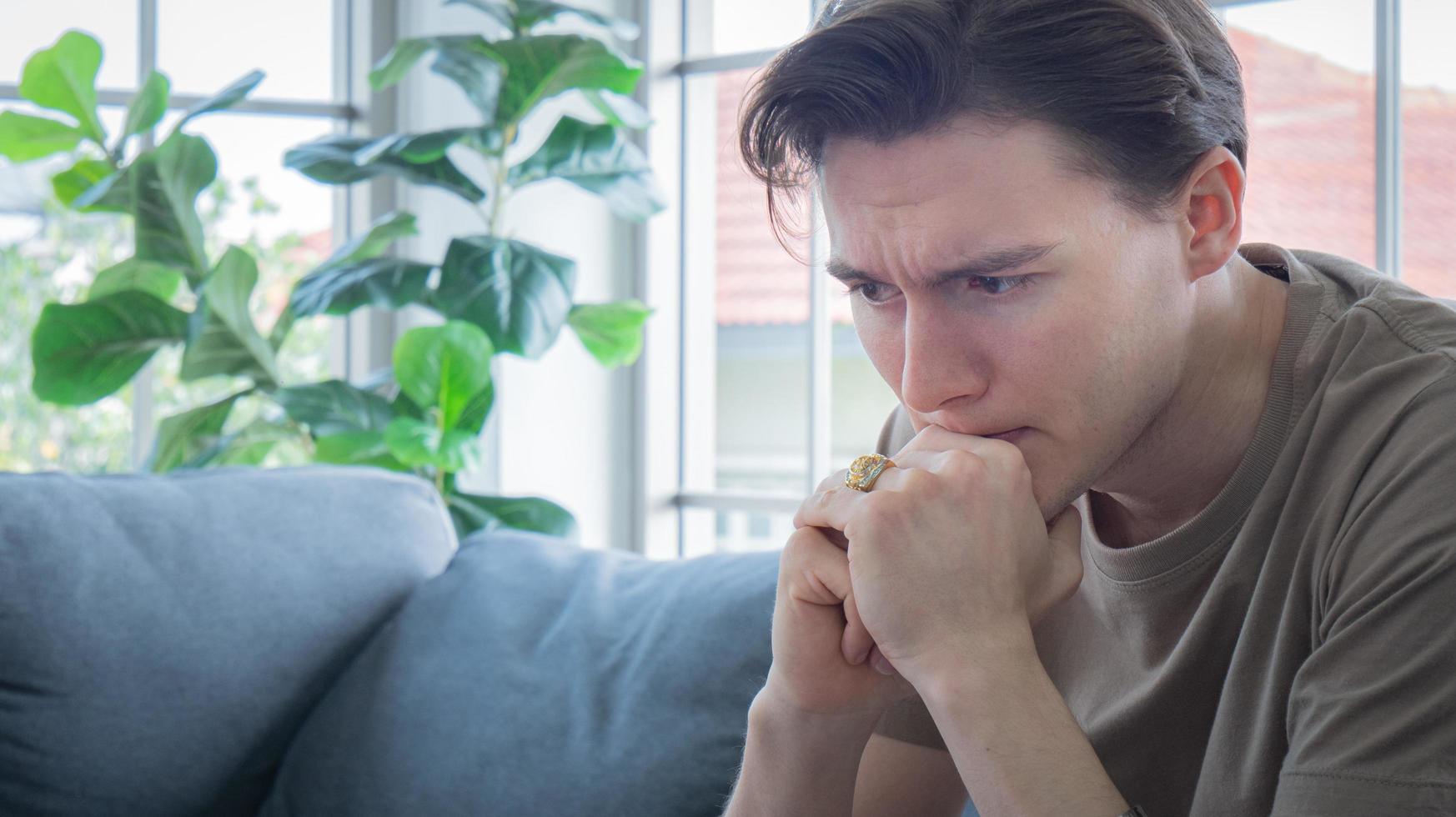 Close up handsome young man Anxious, worried, and bored expression. A young man sits and works in a work-from-home manner, but becomes bored and worried, possibly due to depression. photo