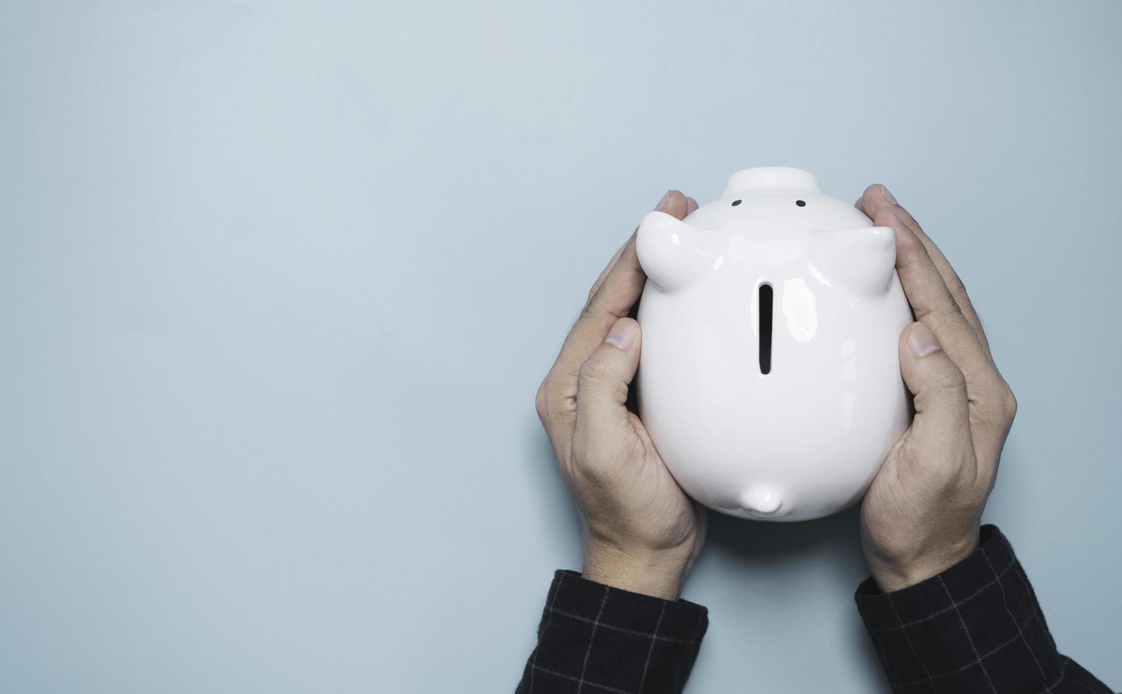 Businessman holding white piggy bank saving on blue background and copy space for deposit and money saving investment concept. photo