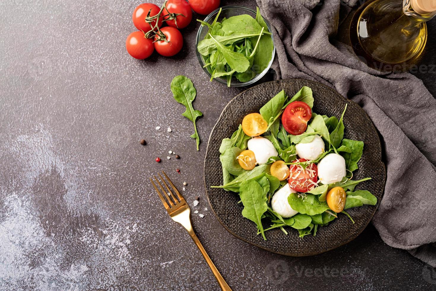 ensalada fresca con rúcula, tomates cherry, queso mozzarella y queso duro sobre fondo oscuro. vista superior foto